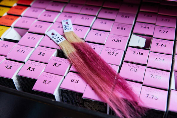 Nachaufnahme pinkfarbener Produktpackungen von professioneller ALCINA Haarfarbe mit oben zwei aufliegenden, pink eingefärbten Haarsträhnen.