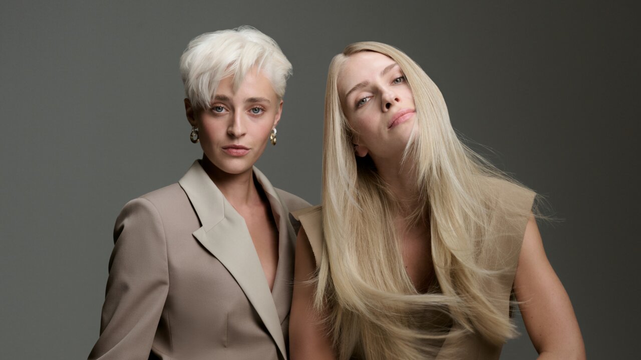 Zwei Models mit blonden Haarvarianten – ein kurzer platinblonder Pixie-Cut und glattes, langes Haar in warmem Blond – präsentieren vielfältige Blondtöne vor einem dunkelgrauen Hintergrund.