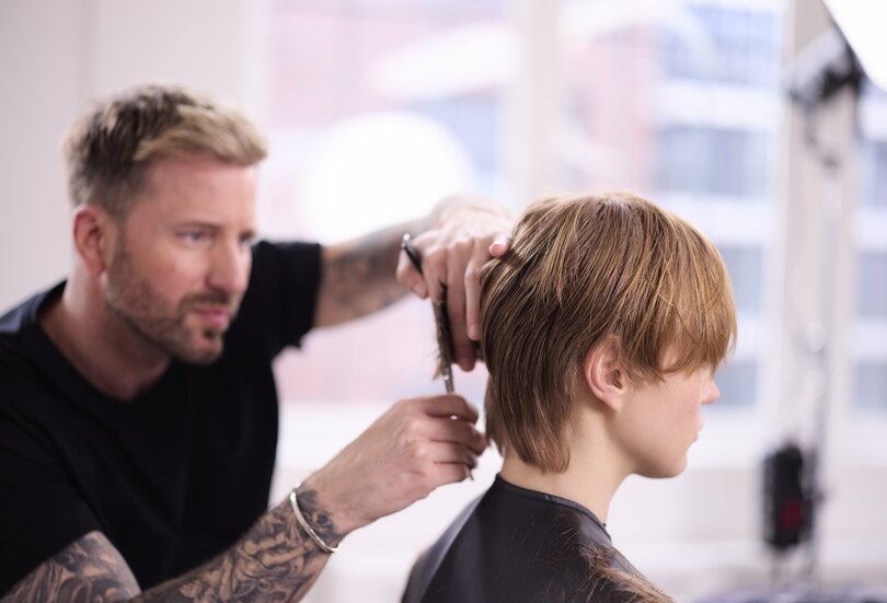 ALCINA Brand Ambassador Robert Mrosek schneidet konzentriert und präzise einen kurzen Haarschnitt bei einem Model.