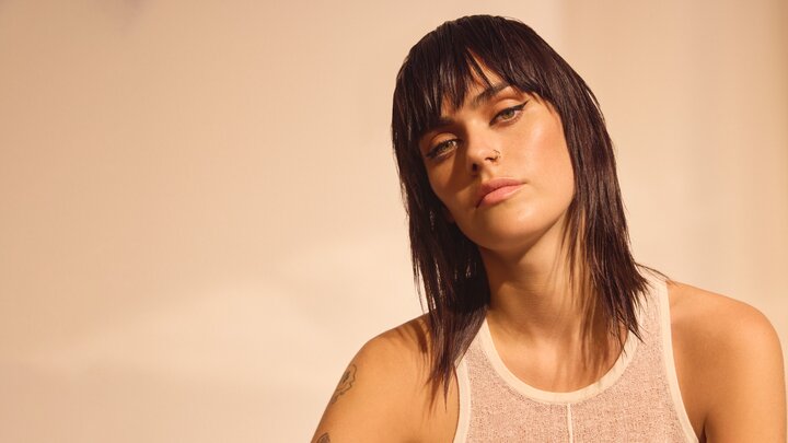 Junge Frau mit kinnlangem, dunkelbraunem Haar und fransig geschnittenem Pony blickt nachdenklich zur Seite und trägt ein schlichtes weißes Tanktop für einen minimalistisch-coolen Look.