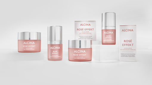 Zwei Tiegel Alcina Rosé Effekt Tagescreme mit Farbpigmenten und Umverpackung plus 2 Pumpspender Alcina Augencreme mit Concealer-Wirkung plus Umverpackung auf Podesten drapiert