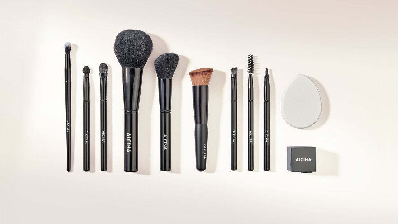 ALCINA Make-up-Zubehör mit verschiedenen Pinseln, Wimpernbürste, Schwämmchen und Kosmetikspitzer, ordentlich nebeneinander angeordnet.