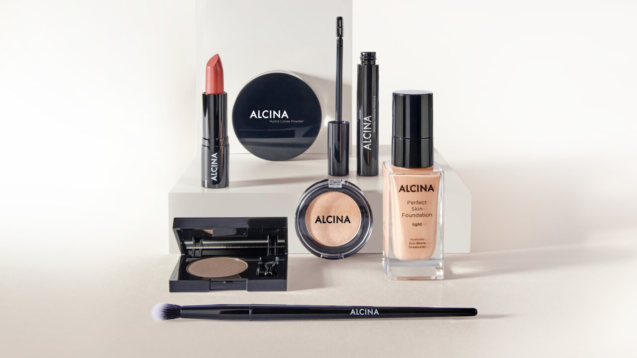 ALCINA Make-up Core Line Produkte mit Foundation, Kompaktpuder, Concealer, Mascara, Lippenstift, Lidschatten und Präzisionspinsel, übersichtlich vor hellem Hintergrund arrangiert für einen vollständigen Teint- und Augen-Make-up-Look.
