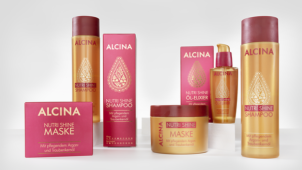 ALCINA Nutri Shine Haarpflegeserie mit Shampoo, Maske und Öl-Elixier in gold-roter Verpackung mit orientalisch inspiriertem Ornament, prominent auf heller Fläche präsentiert.