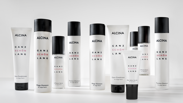 ALCINA „Ganz schön lang“-Pflegeserie für langes Haar in schlichtem weiß-schwarzen Design, mit verschiedenen Shampoos, Conditionern und Sprays, die in einer Reihe für eine übersichtliche Produktpräsentation angeordnet sind.