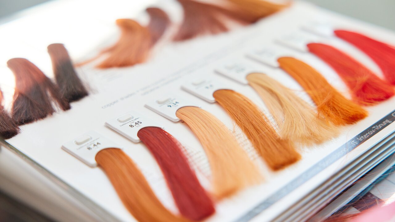 Nahaufnahme eines aufgeschlagenen Farbbuchs, wie es in Friseursalons zum Einsatz kommt. Mit gefärbten Haarsträhnen in verschiedenen Rottönen.