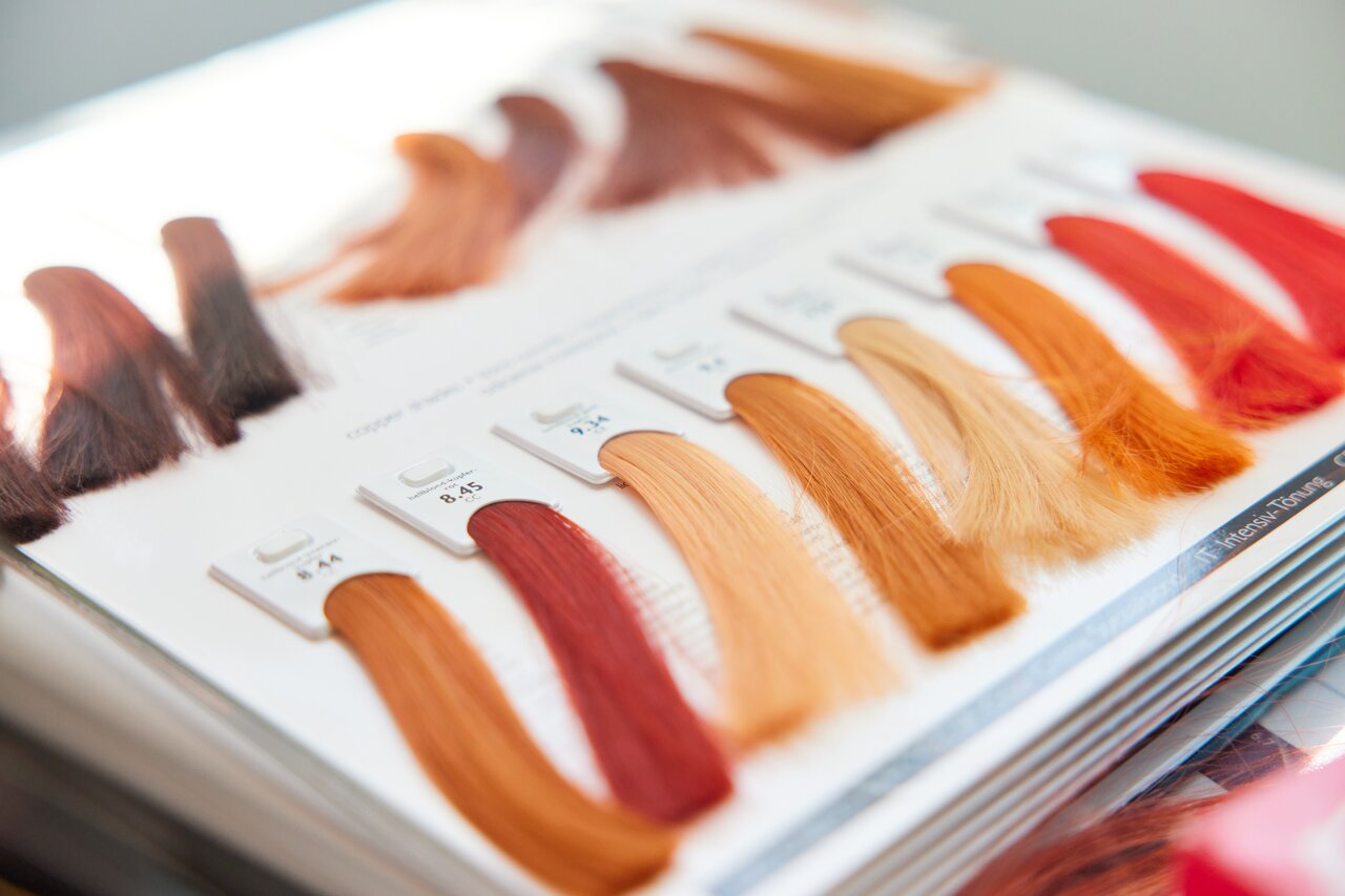 Nahaufnahme eines aufgeschlagenen Farbbuchs, wie es in Friseursalons zum Einsatz kommt. Mit gefärbten Haarsträhnen in verschiedenen Rottönen.