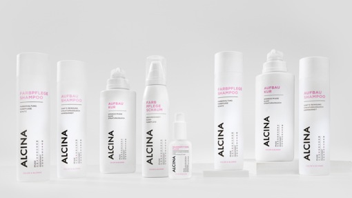 ALCINA Color und Blonde Haarpflegeserie mit Farbpflege-Shampoo, Aufbau-Kur, Aufbau-Shampoo und weiteren Produkten in weiß-pinkem, minimalistischem Design, übersichtlich auf heller Fläche arrangiert.