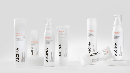 ALCINA Repair-Haarpflegeserie mit Repair-Shampoo, Mousse und Maske in weißem, cleanem Verpackungsdesign, modern auf heller Fläche arrangiert.